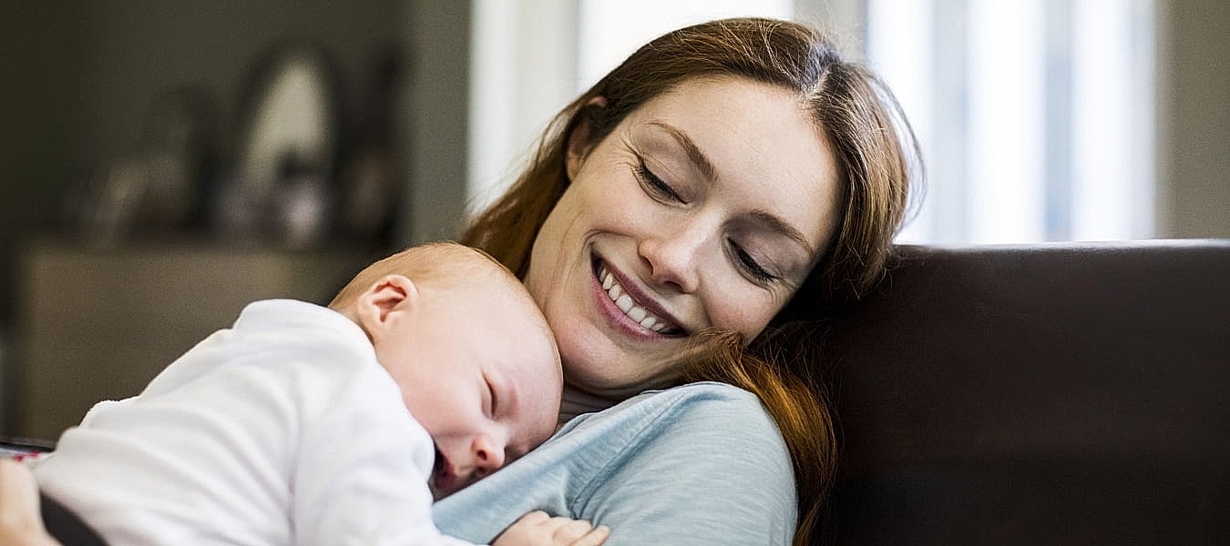 Mother holding sleeping baby, smiling together.