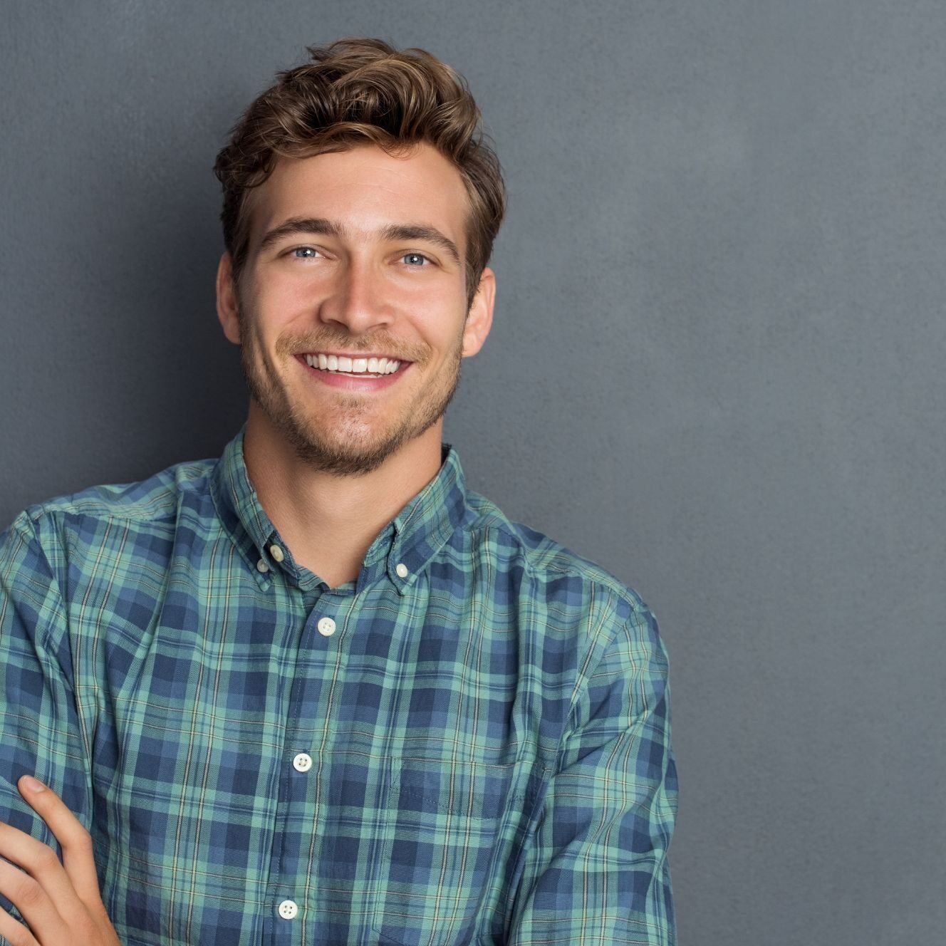 Smiling man in plaid shirt against gray background.