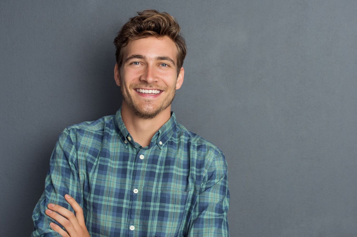 Smiling man in plaid shirt against gray background.