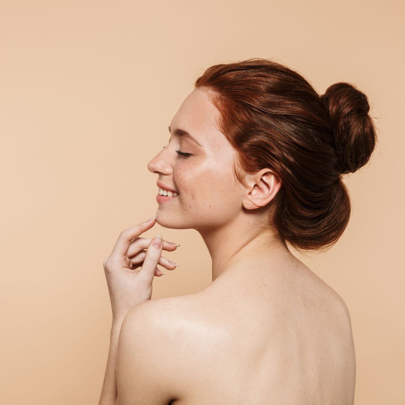 Woman smiling with a bun against a beige background.