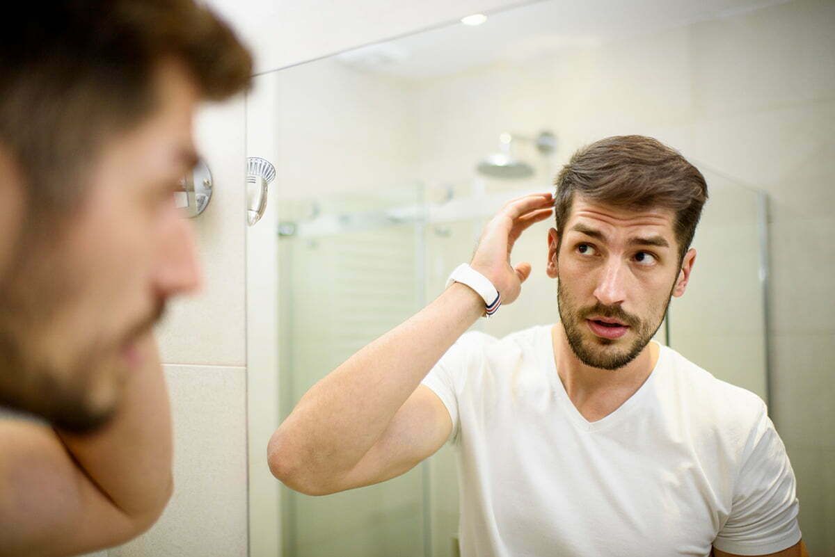 Man styling hair in bathroom mirror.