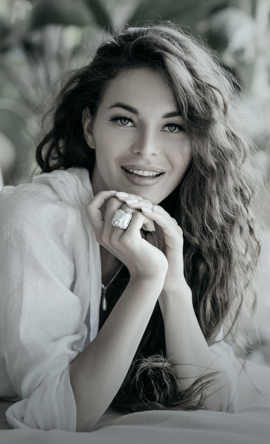 Smiling Denver plastic surgery model with curly hair and jewelry.