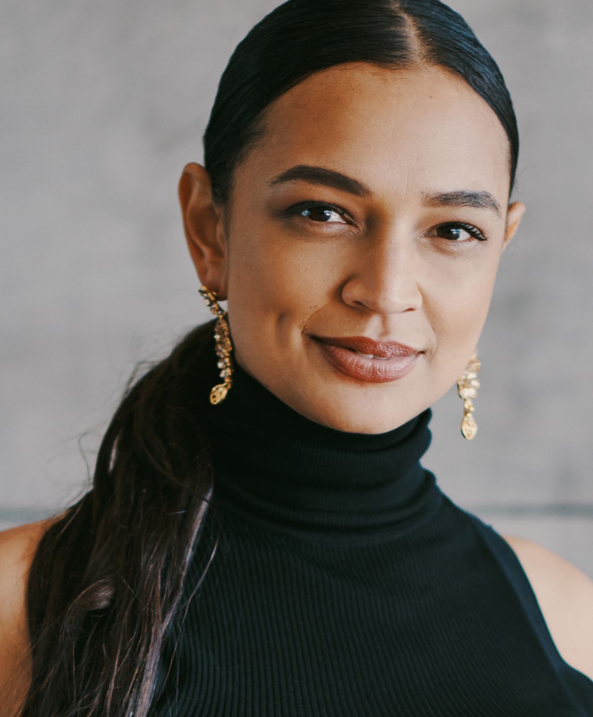 Woman with earrings and a black turtleneck.