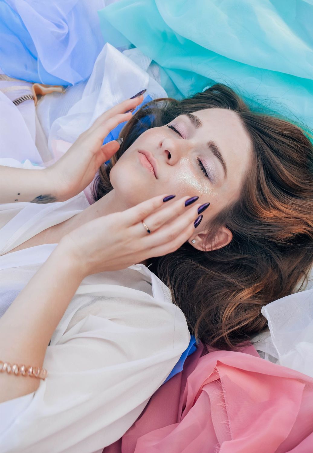 Woman relaxing among colorful fabrics with closed eyes.