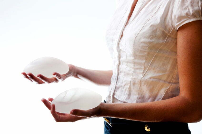 Woman holding silicone breast implants in each hand.