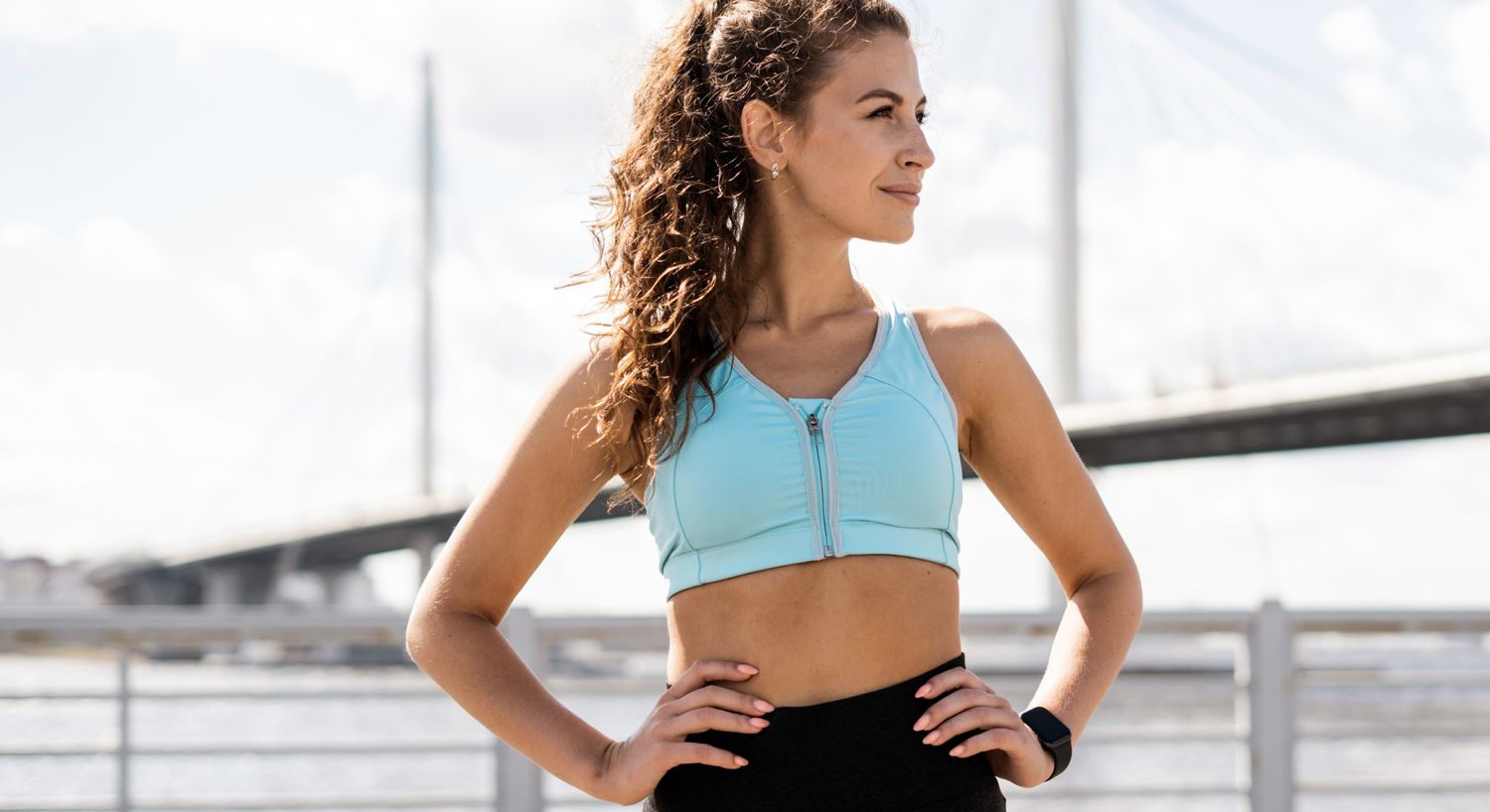 Woman in activewear by waterfront bridge.